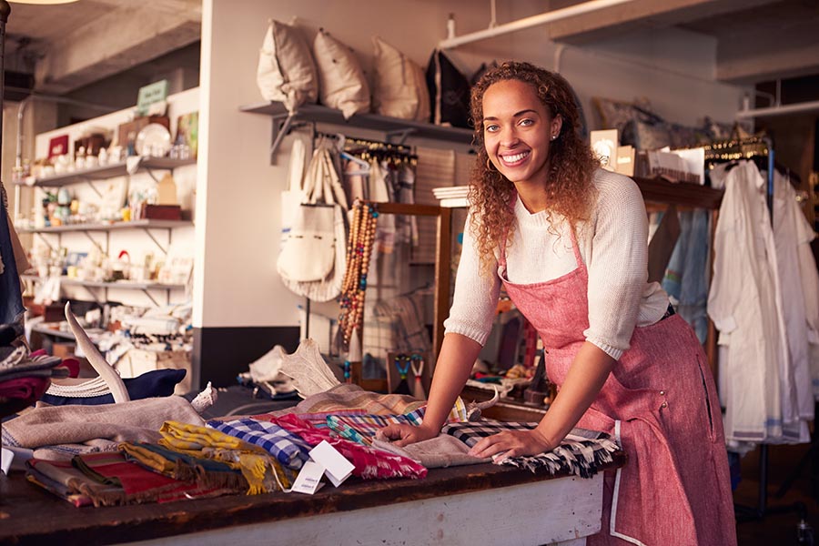 Business Insurance - Shop Owner Organizes Scarves for Sale in a Boutique Filled With Homegoods and Clothing