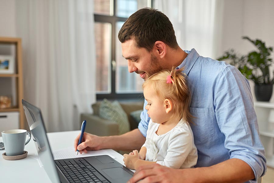 Client Center - Dad in Nice Living Room Uses Computer and Takes Notes, Young Daughter in His Lap