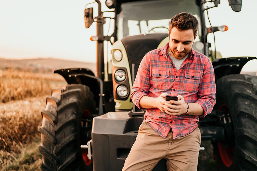 Contact Us - Young Farmer Leans Against Tractor in a Field, Making a Phone Call
