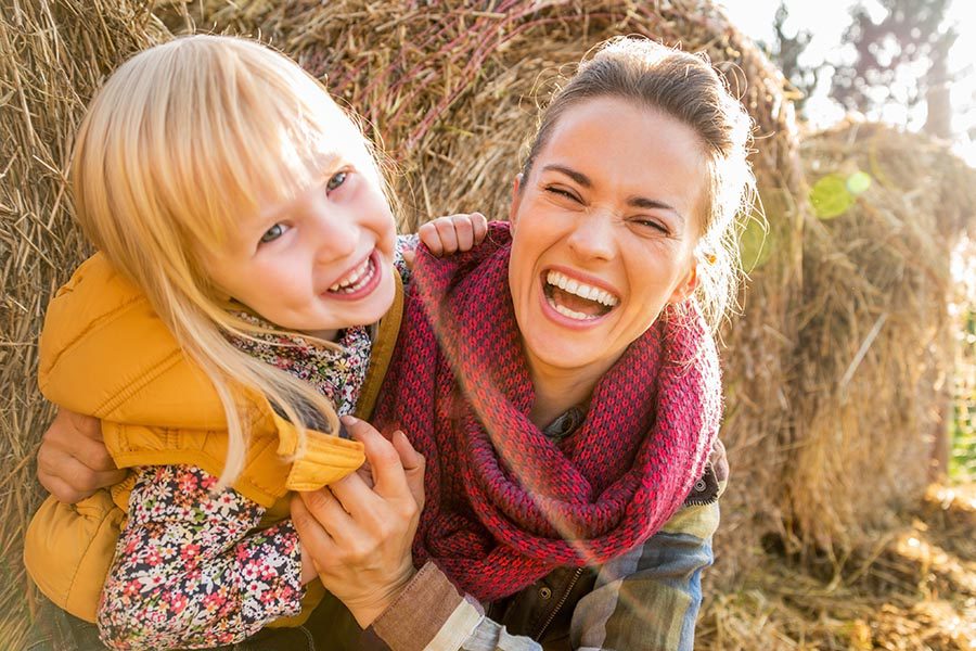 Personal Insurance - Mother and Young Daughter Sit in Front of Hay Bales, Smiling and Hugging, Wearing Fall Clothing